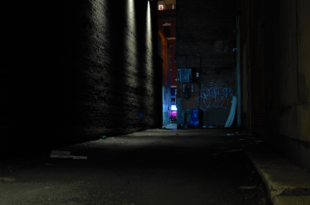 A dark alley lit by a blue light at the far end.
